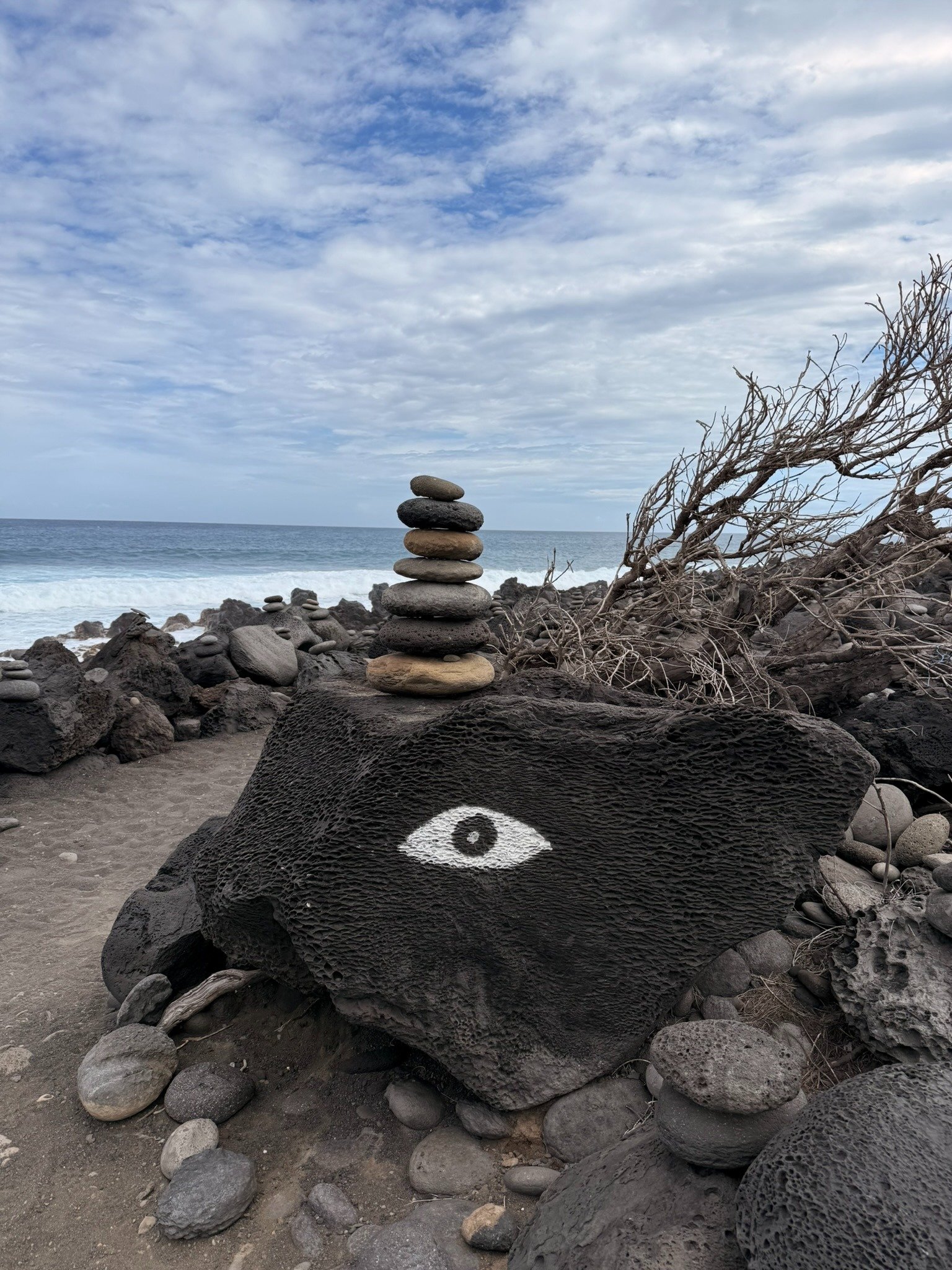 Œil peint sur une roche volcanique à côté d’un cairn sur le sable noir d’Étang-Salé, La Réunion